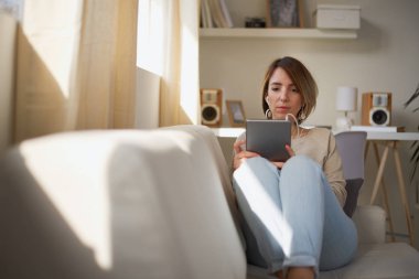 Genç güzel kadın kanepede oturan ve tablet için coumunication kullanma.