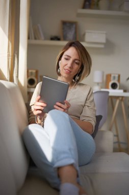 Genç güzel kadın kanepede oturan ve tablet için coumunication kullanma.