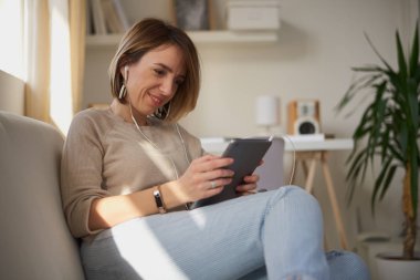 Genç güzel kadın kanepede oturan ve tablet için coumunication kullanma.