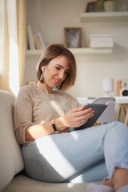 Genç güzel kadın kanepede oturan ve tablet için coumunication kullanma.