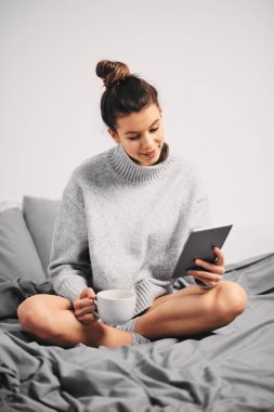 Sabahları yatakta otururken tablet kullanan ve kahve içen kadın portresi