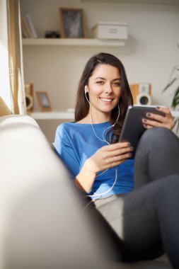 Genç güzel kadın kanepede oturan ve tablet için coumunication kullanma.