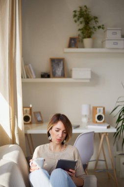 Fincan çay ve dijital tablet ile kanepede oturan genç güzel kadın
