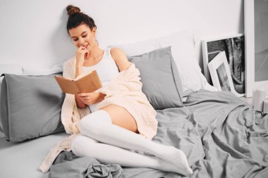 Kız sabah yatakta otururken kitap okuma