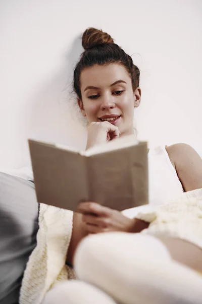 Chica leyendo libro mientras está sentado en la cama por la mañana —  Fotos de Stock