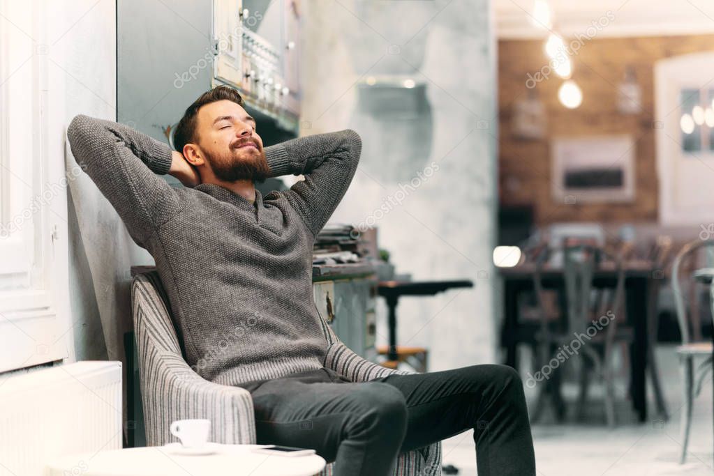 Man resting in the chair at cafe. Hands behind head