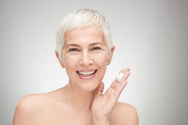 Foto de la cabeza de una hermosa mujer mayor poniéndose la crema . —  Fotos de Stock