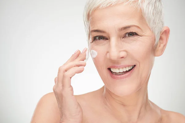 Head shot of beautiful senior woman putting on the creme. — Stock Photo, Image