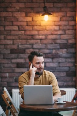Kafede oturan ve akıllı telefon kullanan genç adam.