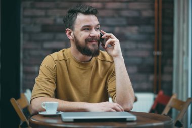 Kafede oturan ve akıllı telefon kullanan genç adam.