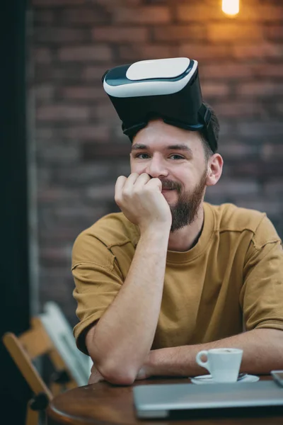 Hombre joven usando caja de realidad virtual mientras está sentado en la cafetería . — Foto de Stock
