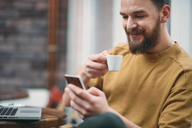 Kafede oturan ve akıllı telefon kullanan genç adam.