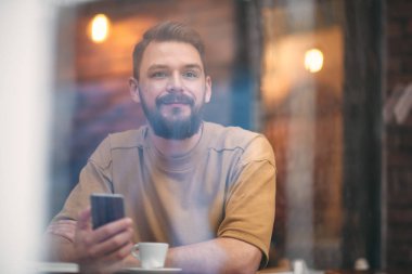 Kafede oturan ve akıllı telefon kullanan genç adam.