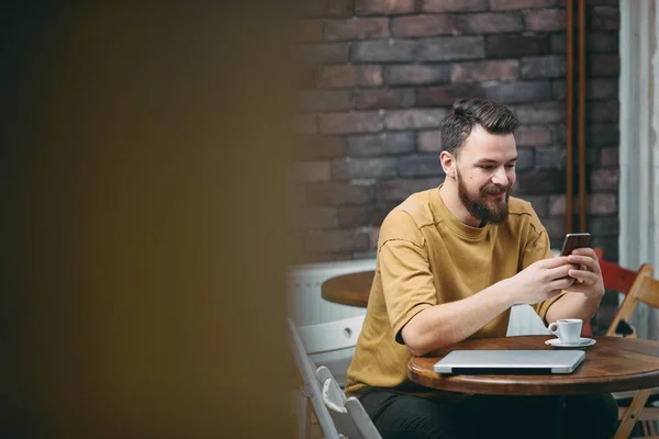 Hombre joven sentado en la cafetería y el uso de teléfono inteligente . — Foto de Stock