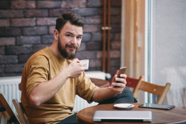 Kafede oturan ve akıllı telefon kullanan genç adam.