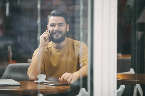 Hombre joven sentado en la cafetería y el uso de teléfono inteligente . — Foto de Stock