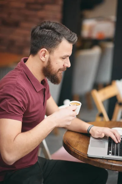 Άνθρωπος πίνει καφέ και χρήση φορητού υπολογιστή ενώ κάθονται στην καφετέρια. — Φωτογραφία Αρχείου