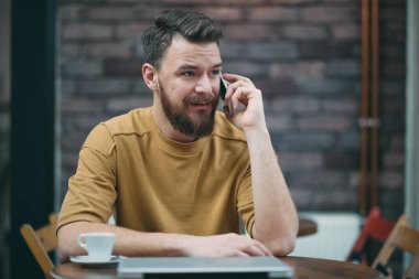 Kafede oturan ve akıllı telefon kullanan genç adam.