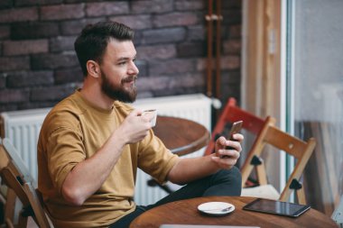 Kafede oturan ve akıllı telefon kullanan genç adam.
