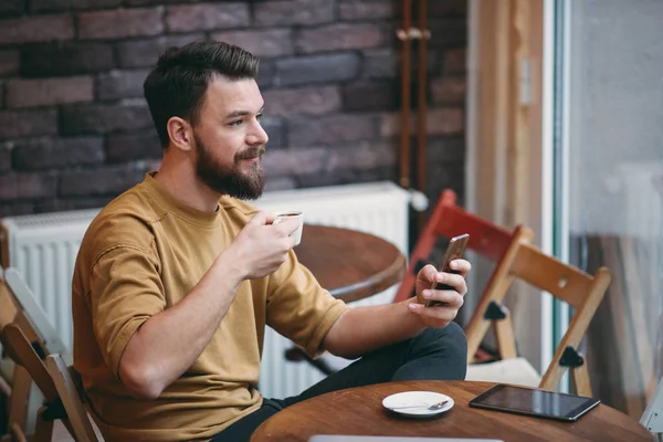 Hombre joven sentado en la cafetería y el uso de teléfono inteligente . — Foto de Stock