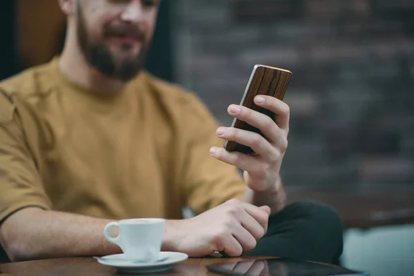 Hombre joven sentado en la cafetería y el uso de teléfono inteligente . — Foto de Stock