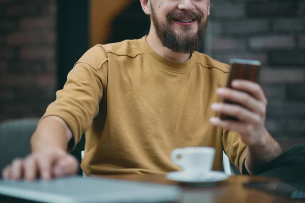 Hombre joven sentado en la cafetería y el uso de teléfono inteligente . — Foto de Stock