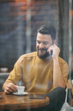 Kafeteryada oturan ve akıllı telefon kullanan genç adam