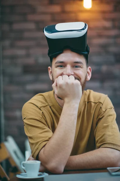 Hombre joven usando caja de realidad virtual mientras está sentado en la cafetería . — Foto de Stock