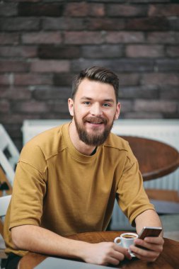 Kafede oturan ve akıllı telefon kullanan genç adam.