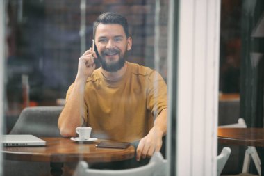 Kafede oturan ve akıllı telefon kullanan genç adam.