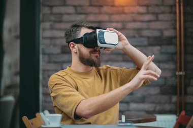 Genç adam kafeteryada otururken sanal gerçeklik kutusunu kullanarak.