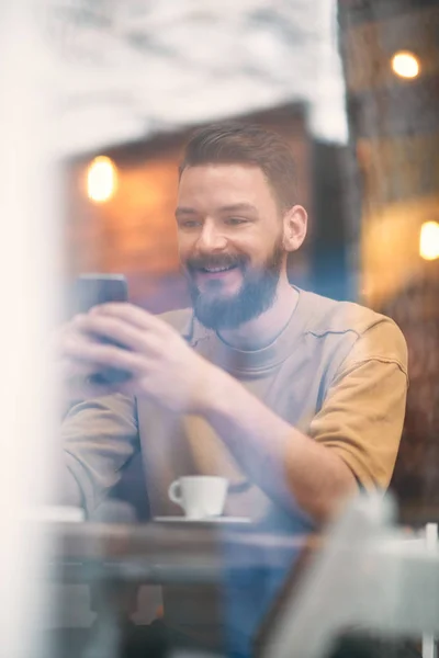 Hombre joven sentado en la cafetería y el uso de teléfono inteligente . — Foto de Stock
