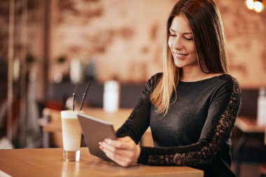 Kafe ve DRI otururken tablet kullanan genç beyaz kadın