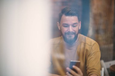 Kafede oturan ve akıllı telefon kullanan genç adam.