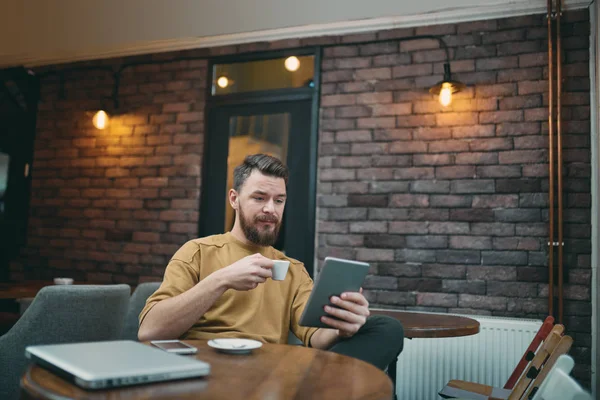 Молодий чоловік сидить у кафетерії і використовує планшетний комп'ютер — стокове фото