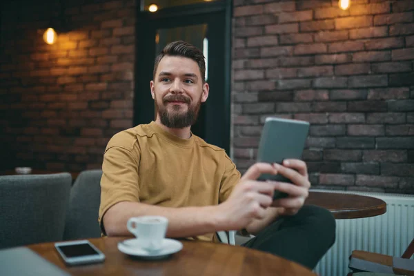 Joven sentado en la cafetería y usando tableta — Foto de Stock