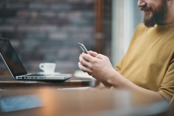Jeune homme assis dans un café et utilisant un téléphone intelligent . — Photo