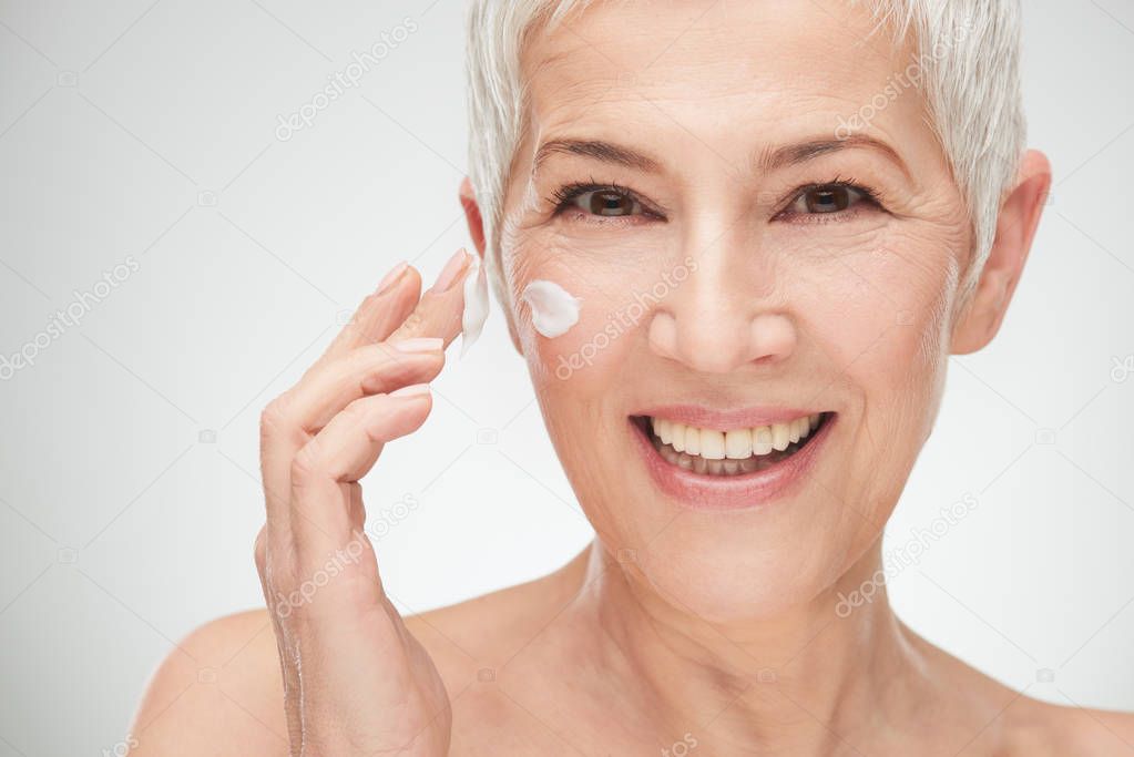 Head shot of beautiful senior woman putting on the cream.