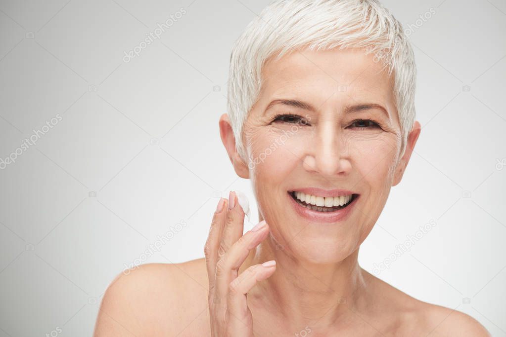 Head shot of beautiful senior woman putting on the cream.