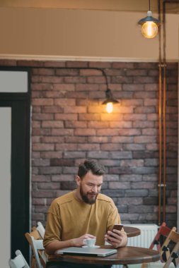 Kafede oturan ve akıllı telefon kullanan genç adam.