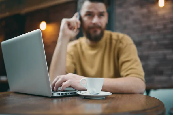 Homem usando laptop e telefone inteligente enquanto sentado no café. Conceito de novas tecnologias — Fotografia de Stock