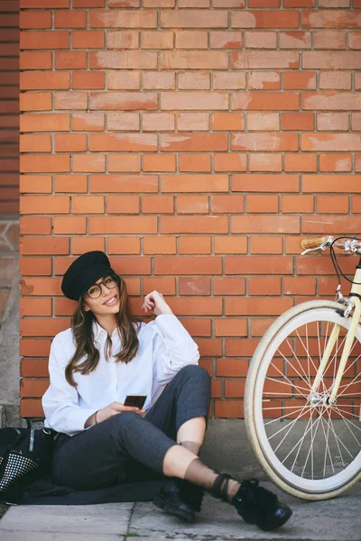 Nő ült a járdán és intelligens telefon használata. Mellett a sárga bicikli. — Stock Fotó