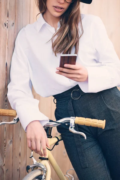 Zbliżenie na kobiecej ręce trzymając smartfon. Selektywny fokus na telefon. Kobieta stojąc przed żółty rower. — Zdjęcie stockowe
