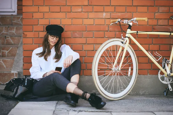 Kaldırımda oturan ve akıllı telefon kullanarak kadın. Yanındaki sarı Onun Bisiklet.