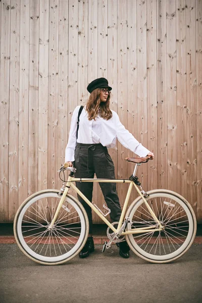 Retrato de una hermosa morena sosteniendo bicicleta. Fondo de madera . —  Fotos de Stock