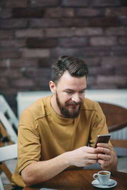 Kafede oturan ve akıllı telefon kullanan genç adam.