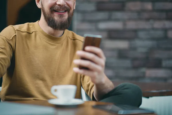 Hombre joven sentado en la cafetería y el uso de teléfono inteligente . — Foto de Stock