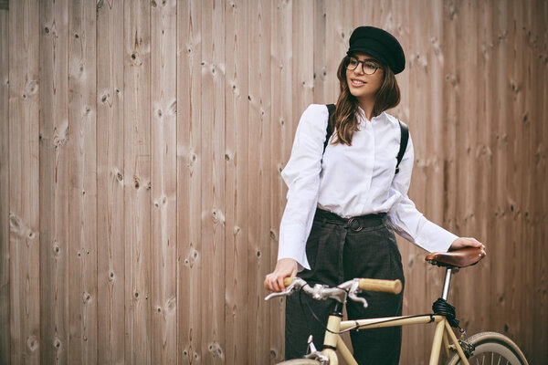 Portrait of beautiful brunette holding bicycle. Wooden background
