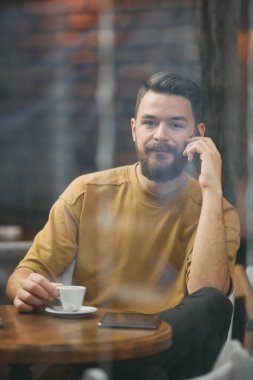 Kafede oturan ve akıllı telefon kullanan genç adam. 