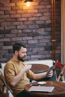 Kafeteryada oturan ve tablet bilgisayarı kullanan genç adam 